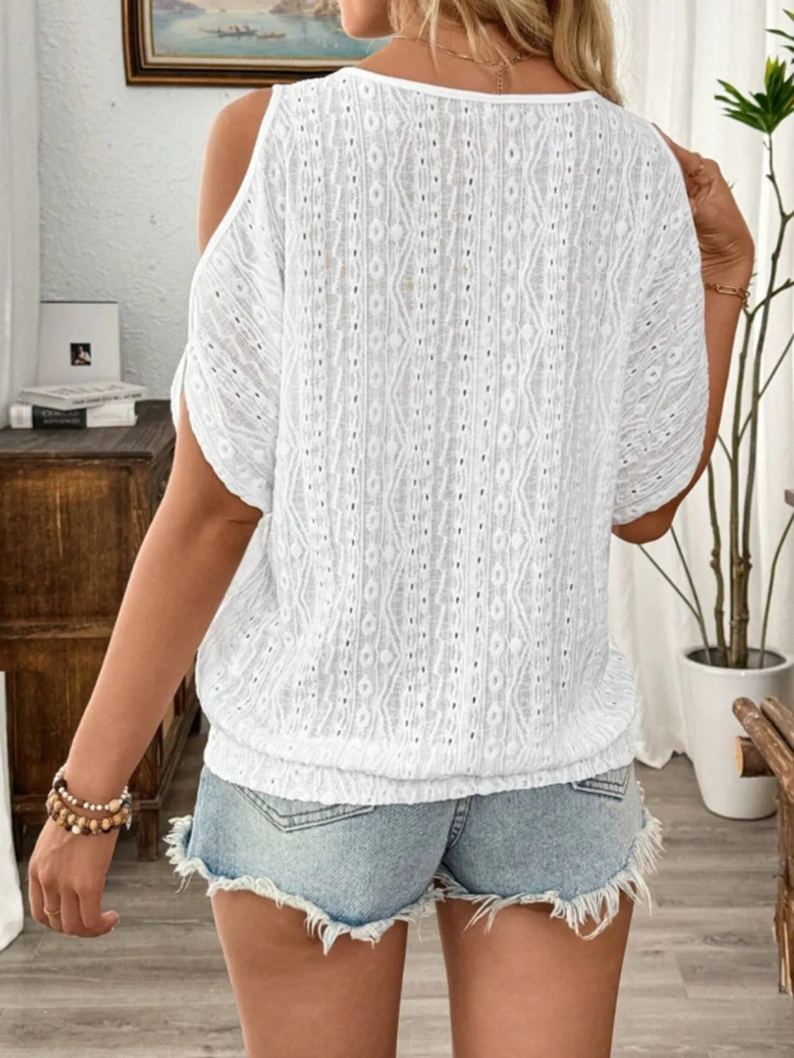 Woman wearing a white textured top and denim shorts in a home setting