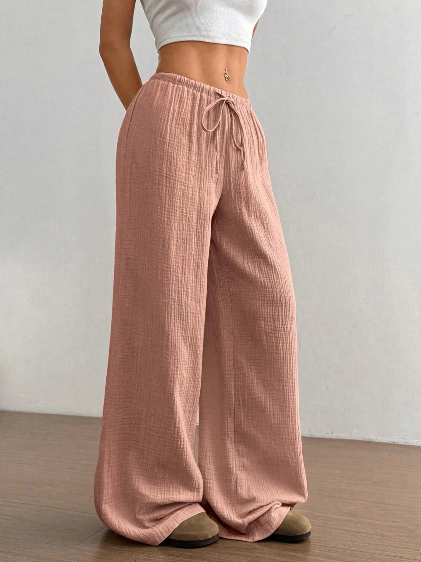 Person wearing pink wide-leg pants with a white top against a plain background