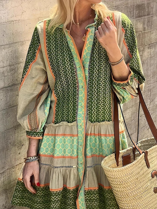 Woman wearing a green and beige patterned dress against a stone wall.