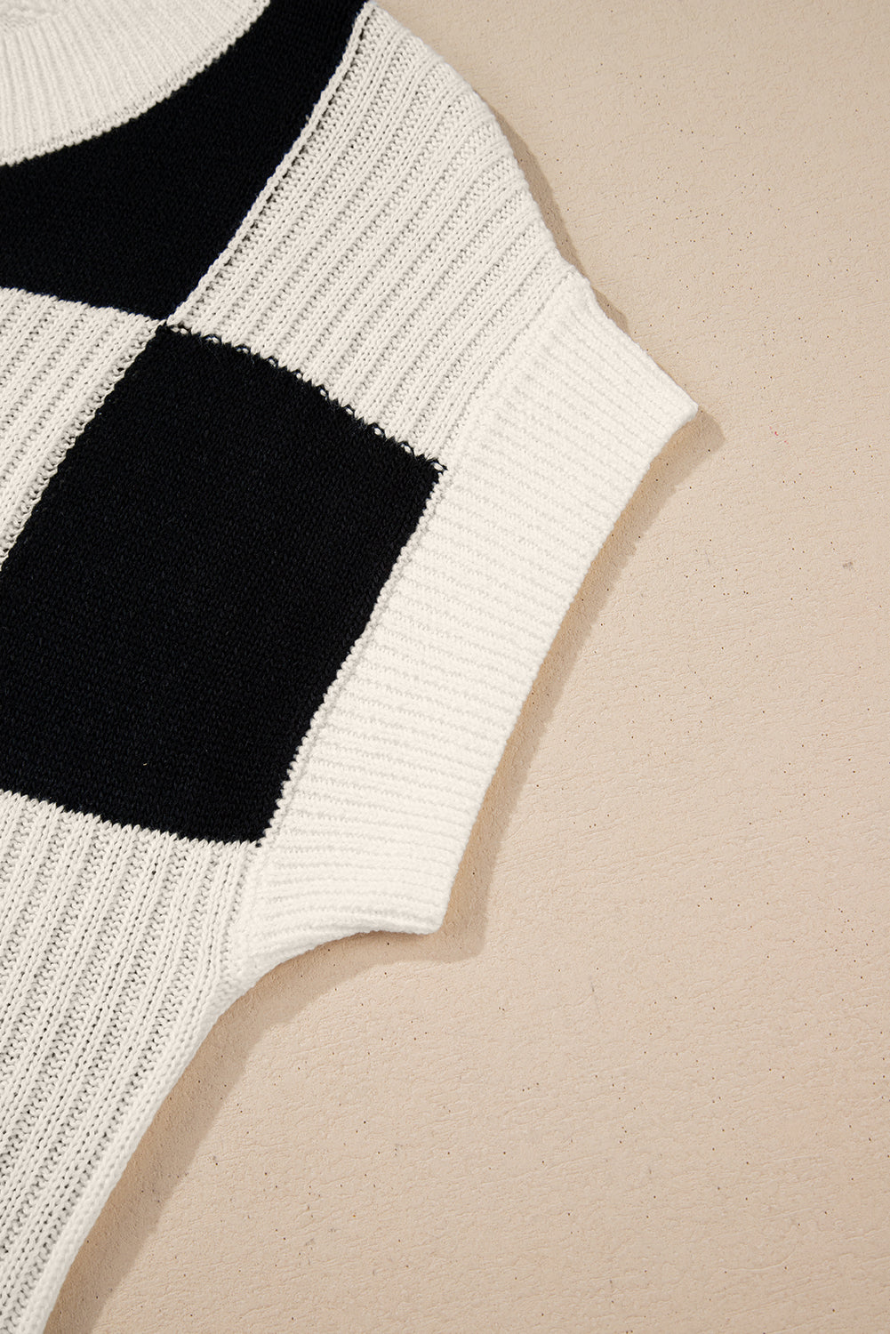 Close-up of a white sweater with black square pattern on a beige background