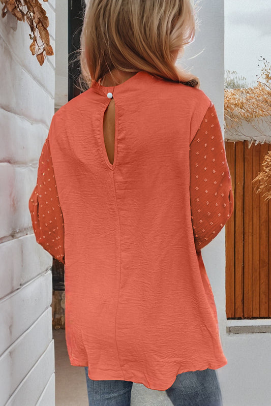 Person wearing an orange polka dot blouse with a white wall and decorative elements in the background