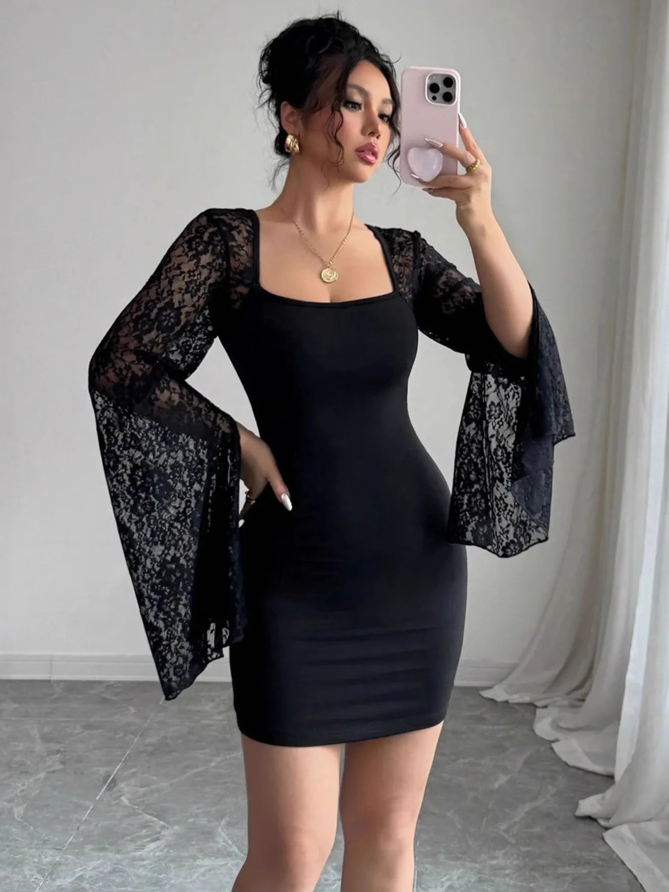 Woman wearing a black dress with sheer sleeves, taking a mirror selfie.