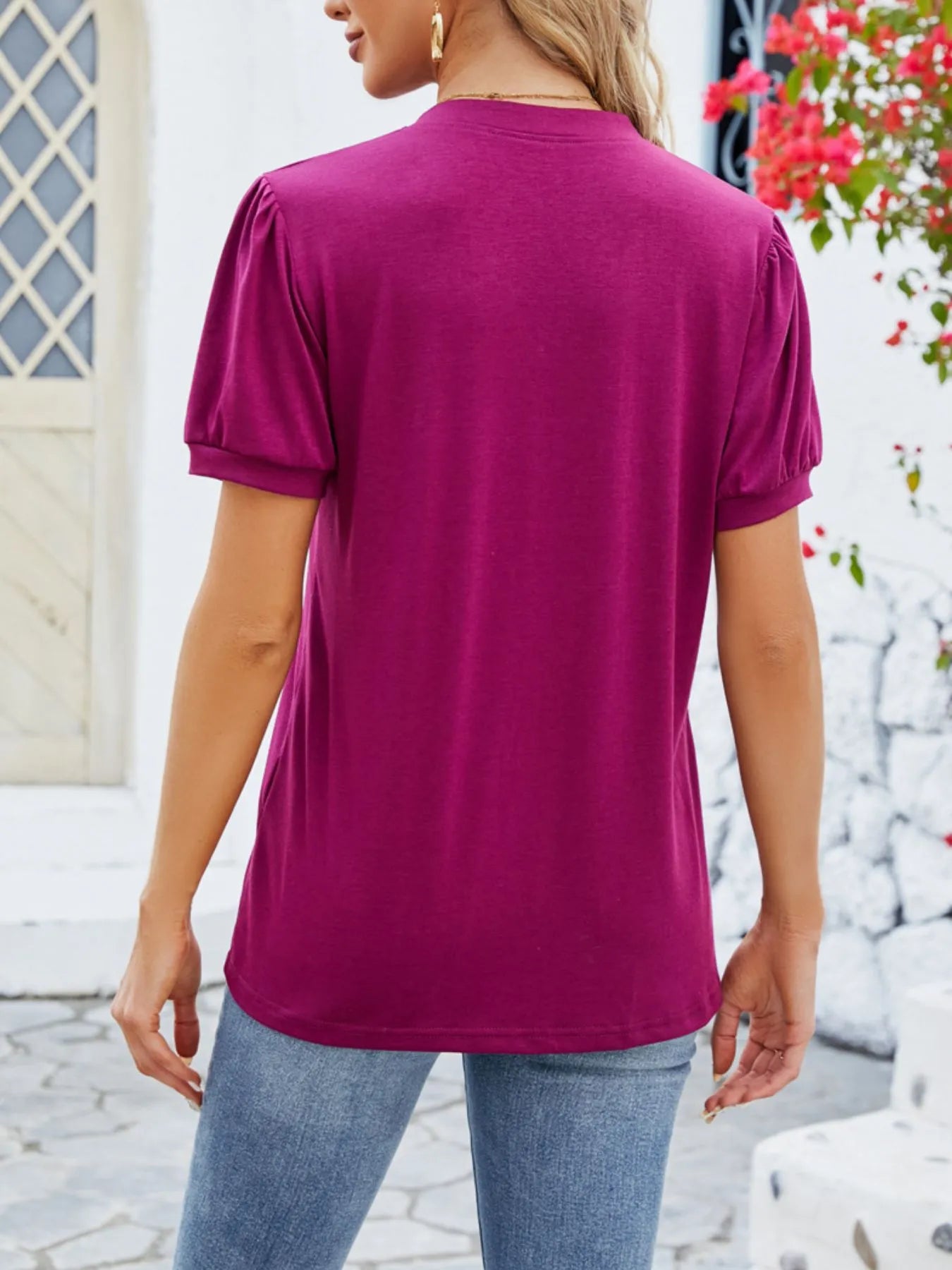 Person wearing a magenta t-shirt and blue jeans standing outdoors.