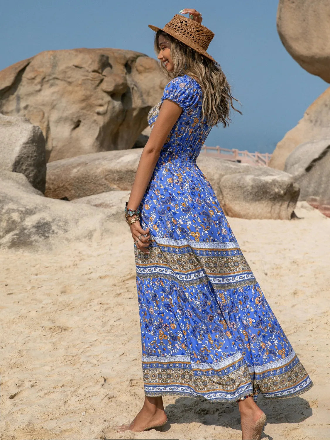 Woman in a blue dress with a pattern standing on rocky terrain.