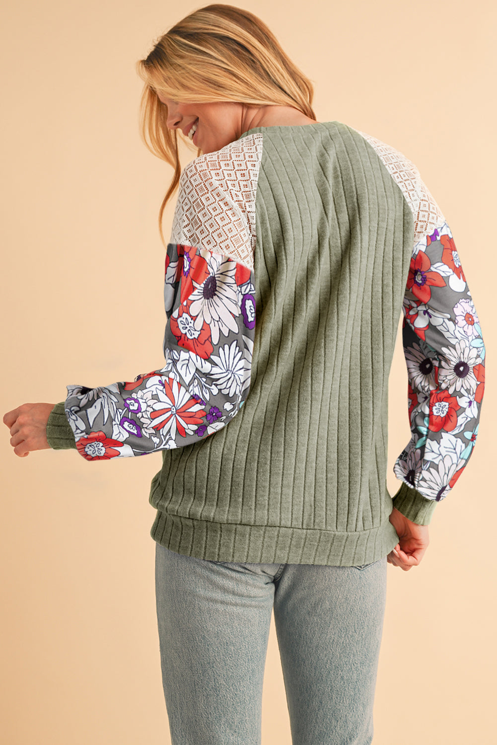 Woman wearing a green sweater with floral-patterned sleeves on a beige background