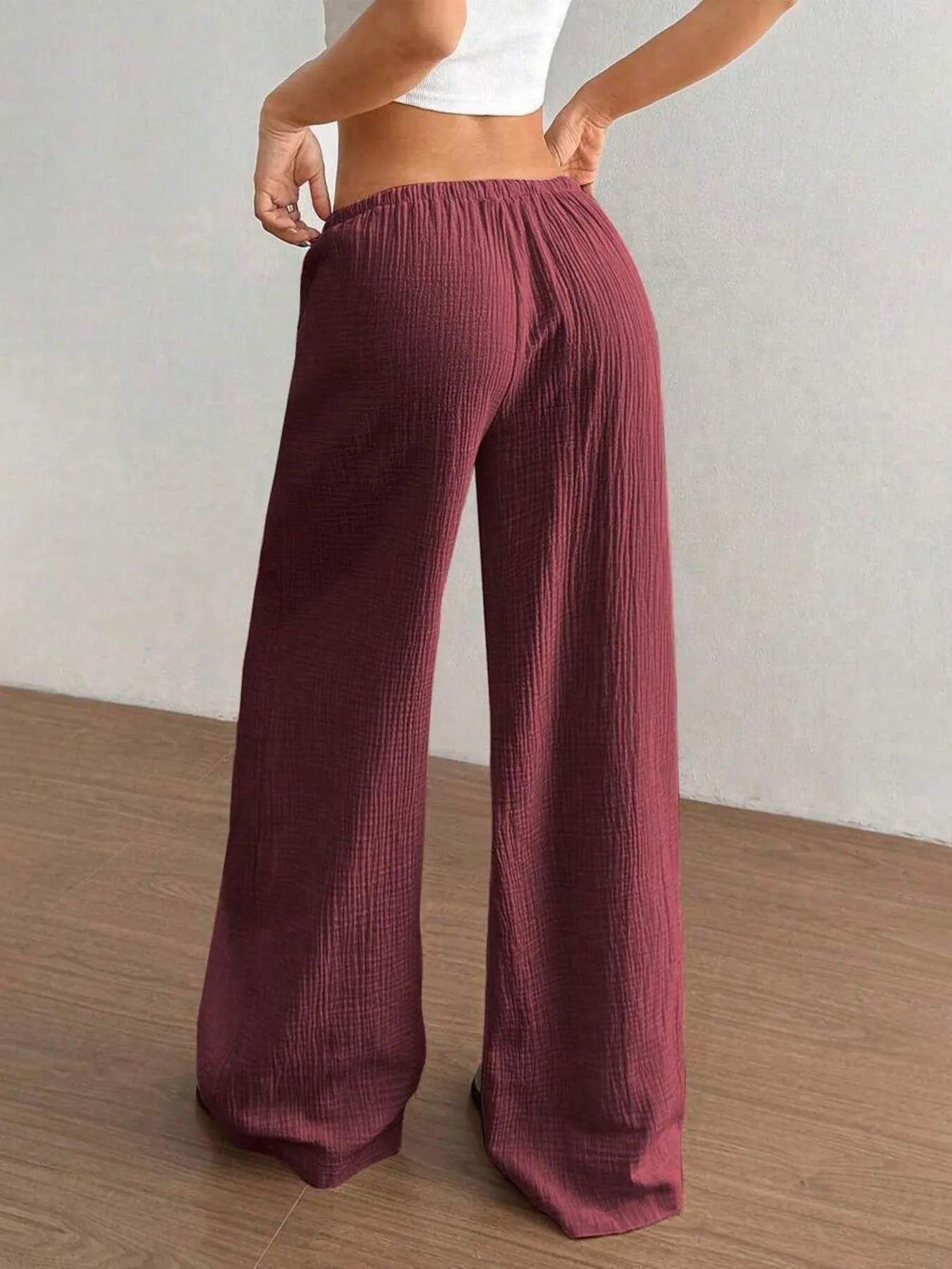 Maroon ribbed wide-leg pants worn by a person on a wooden floor with a white wall background