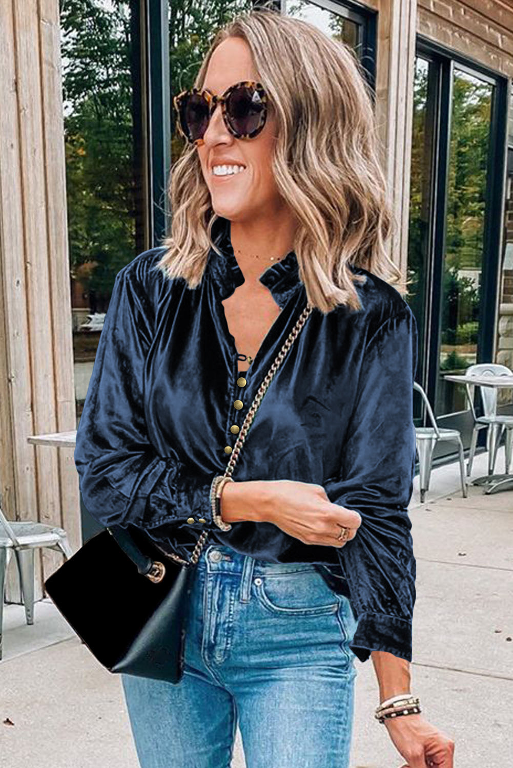 Woman wearing a navy velvet shirt and blue jeans outdoors.