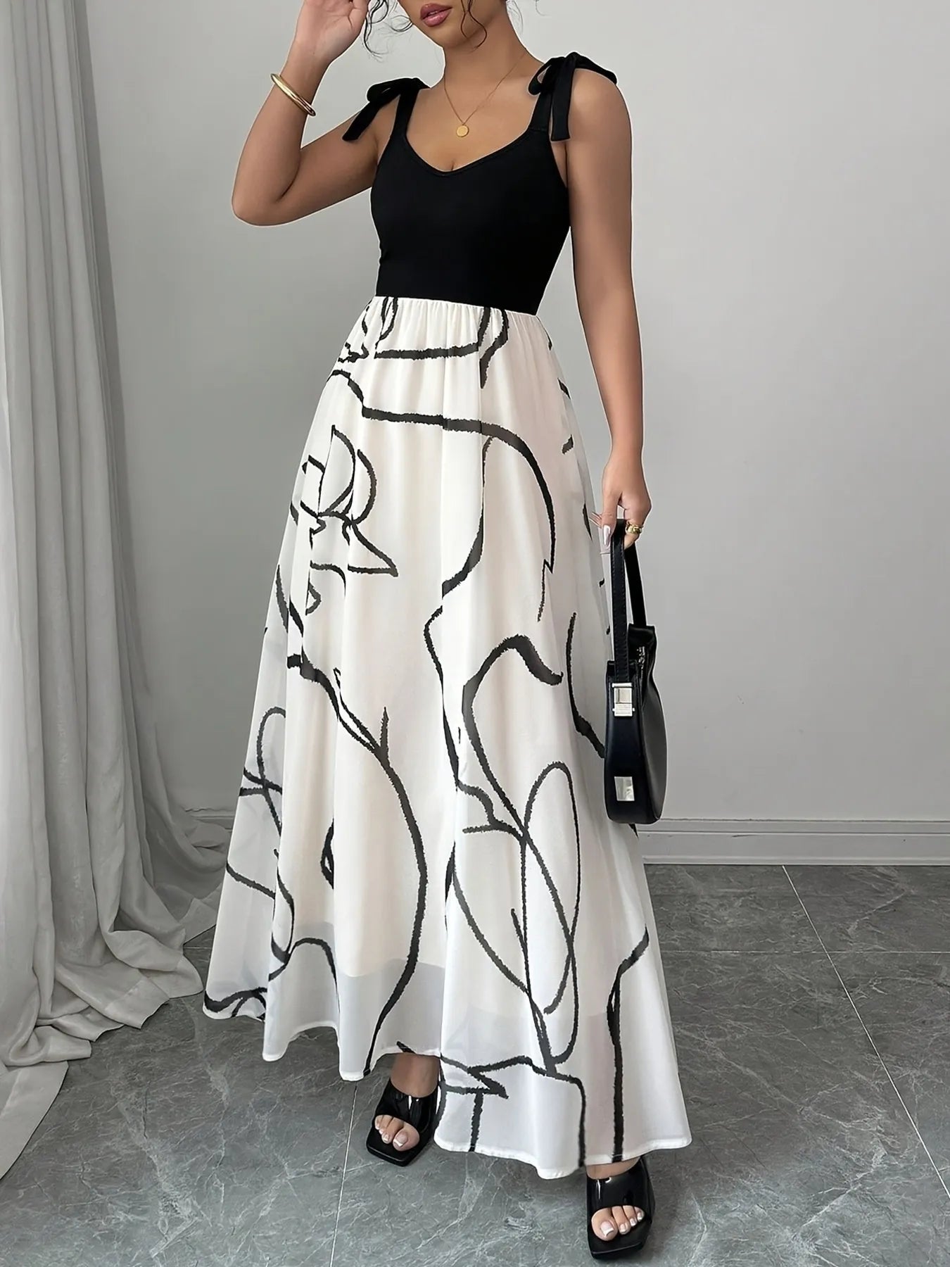 Woman wearing a black top and white skirt with black abstract patterns, holding a black handbag.