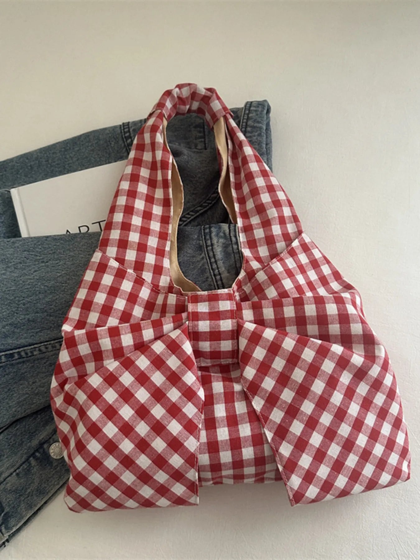 Red and white checkered bag on a white surface with jeans in the background