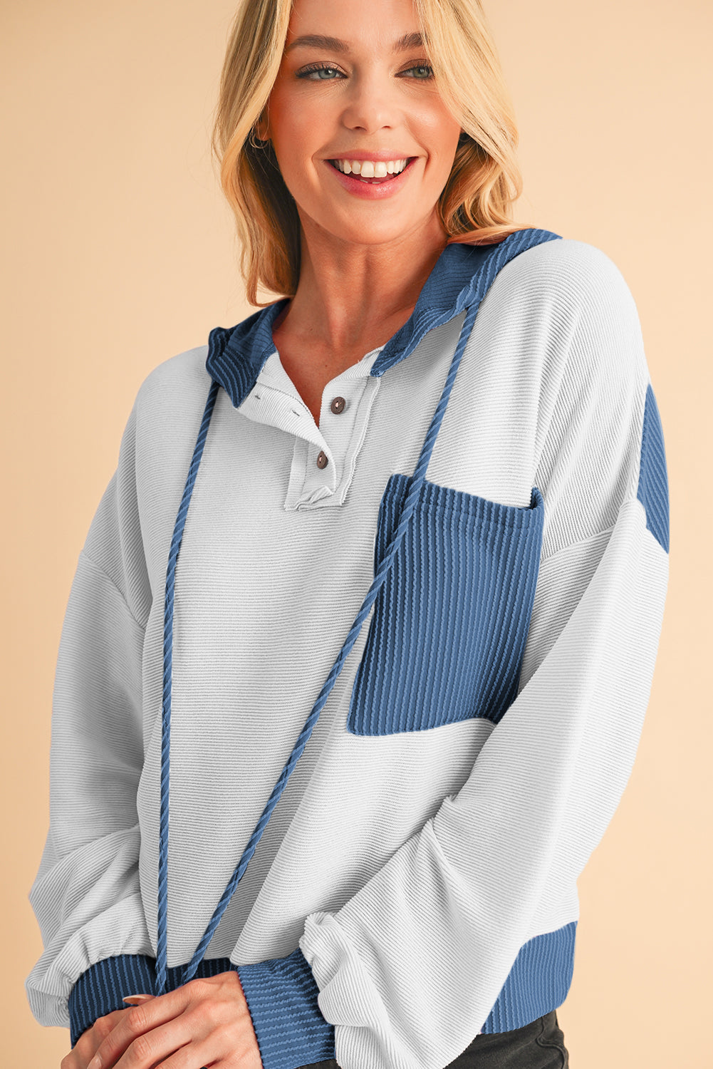 Woman wearing a white and blue color-blocked pullover with a beige background