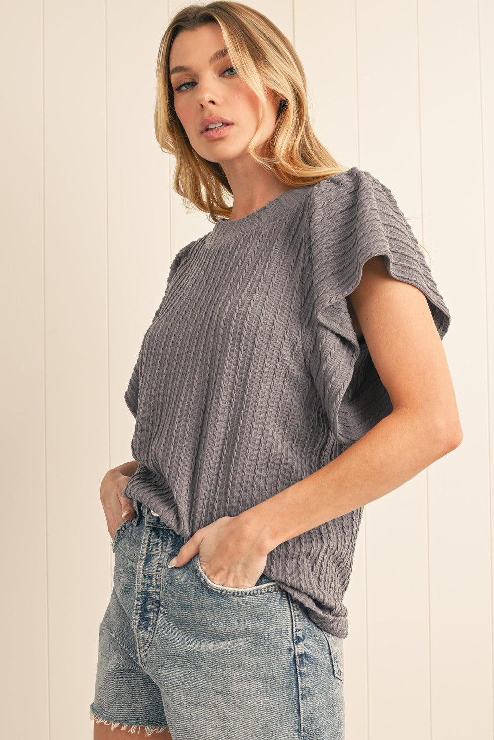 Woman wearing a gray ribbed top and denim shorts against a light background