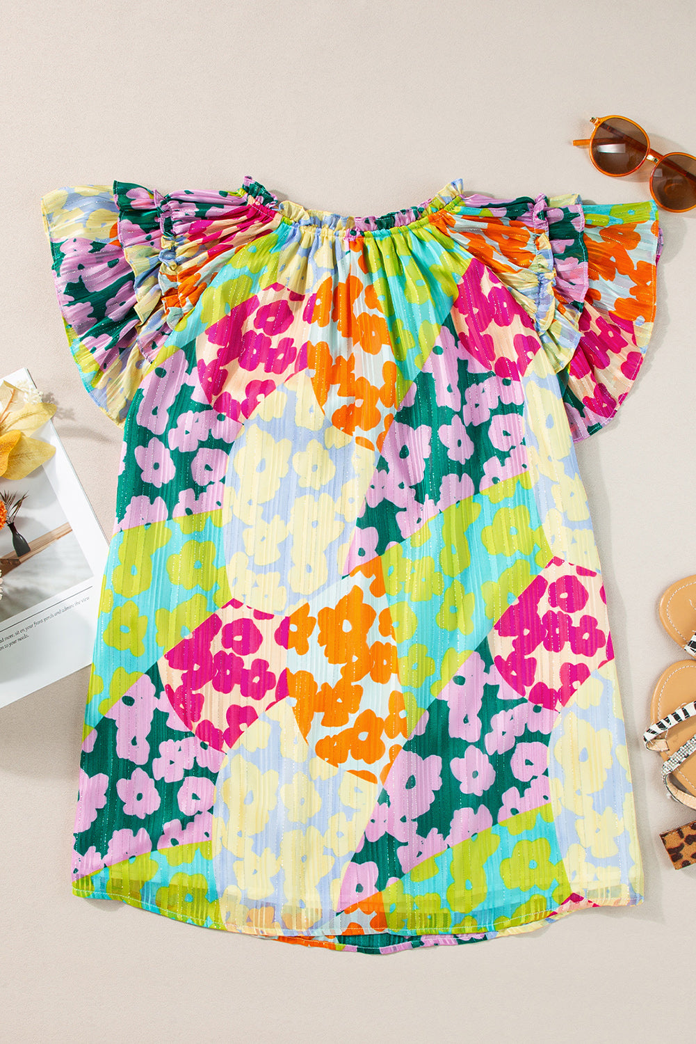 Colorful floral dress on a light background with sunglasses and a magazine.