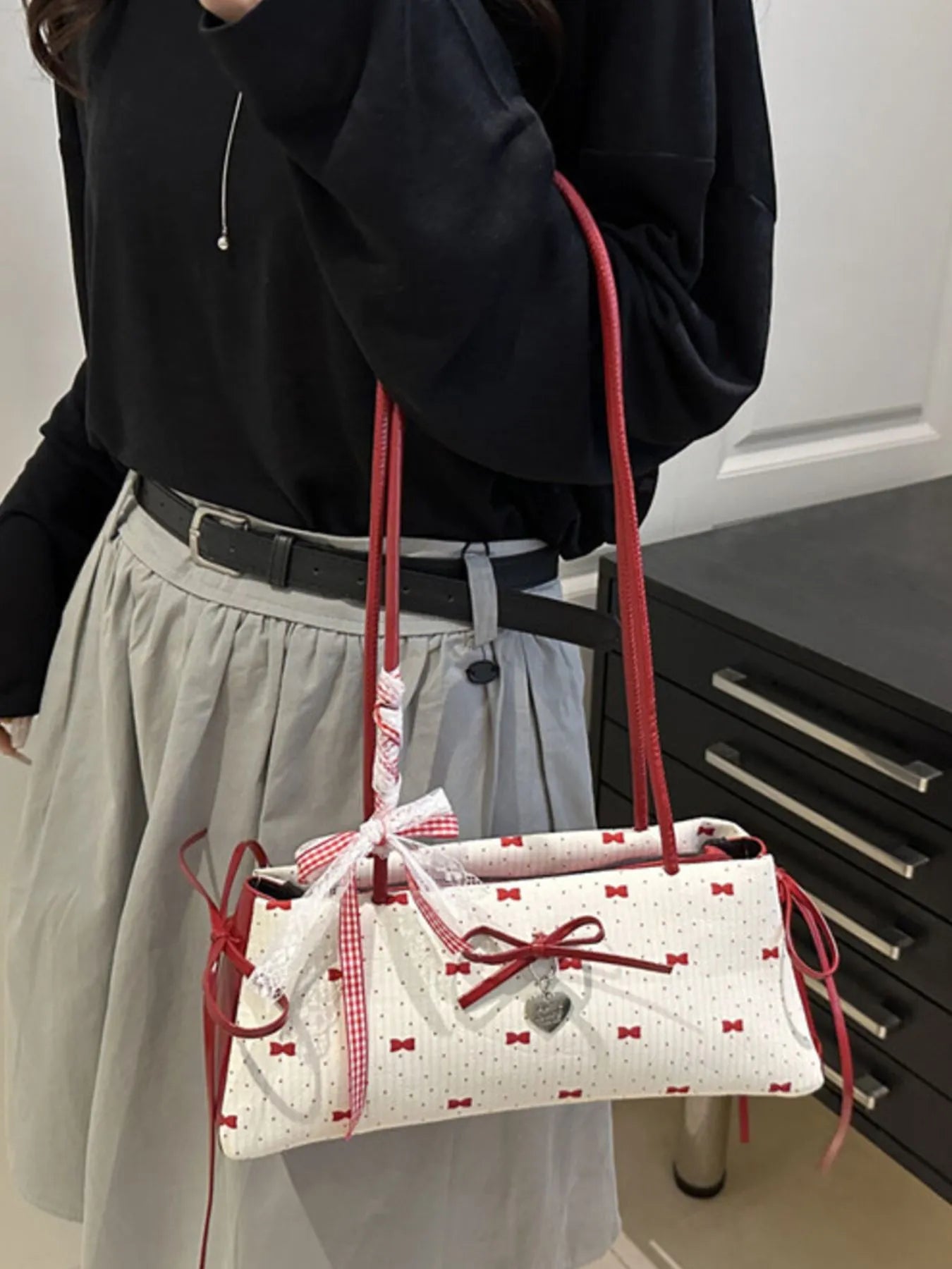 Person holding a white handbag with red accents and bow details.