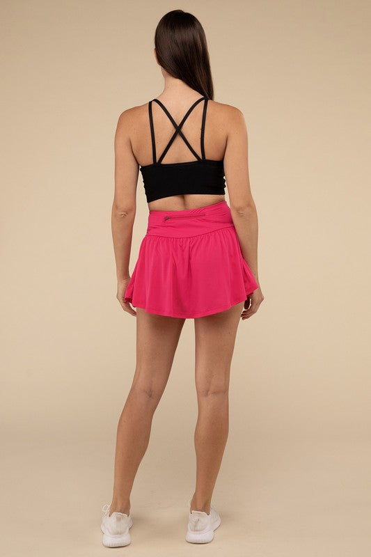 Person wearing a black sports bra and pink tennis skirt on a beige background