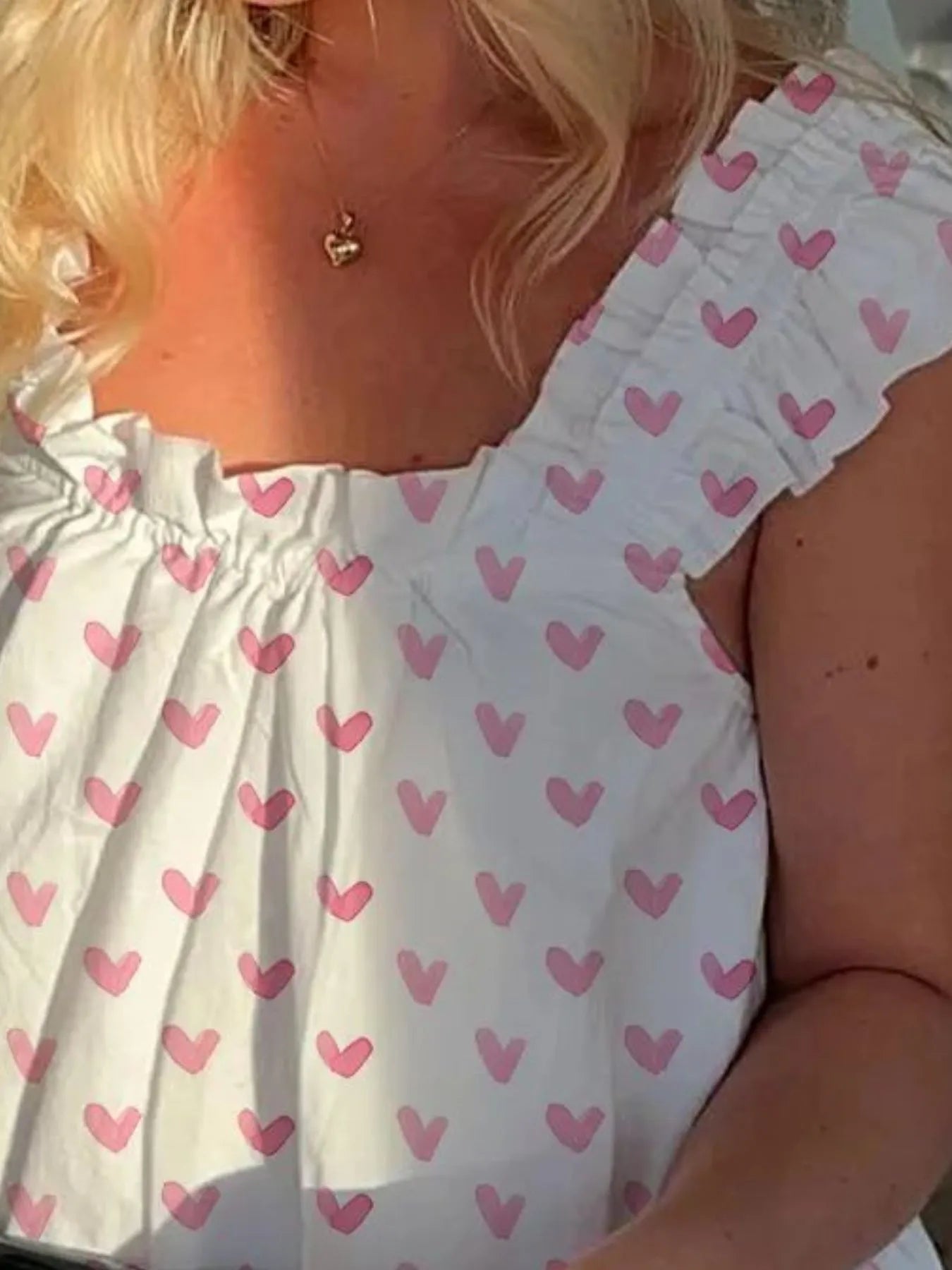 White top with pink heart pattern worn by a person.