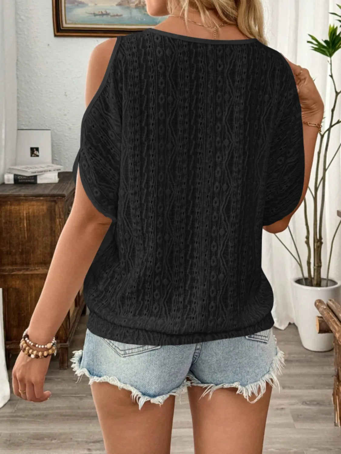 Person wearing a black cable knit sweater and denim shorts in a room with a desk and plant.