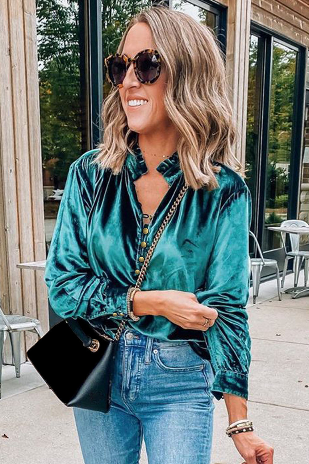 Woman wearing a teal velvet shirt and blue jeans outdoors.