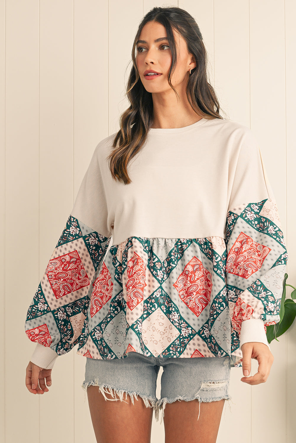 Woman wearing a white top with patterned sleeves against a light wooden panel background