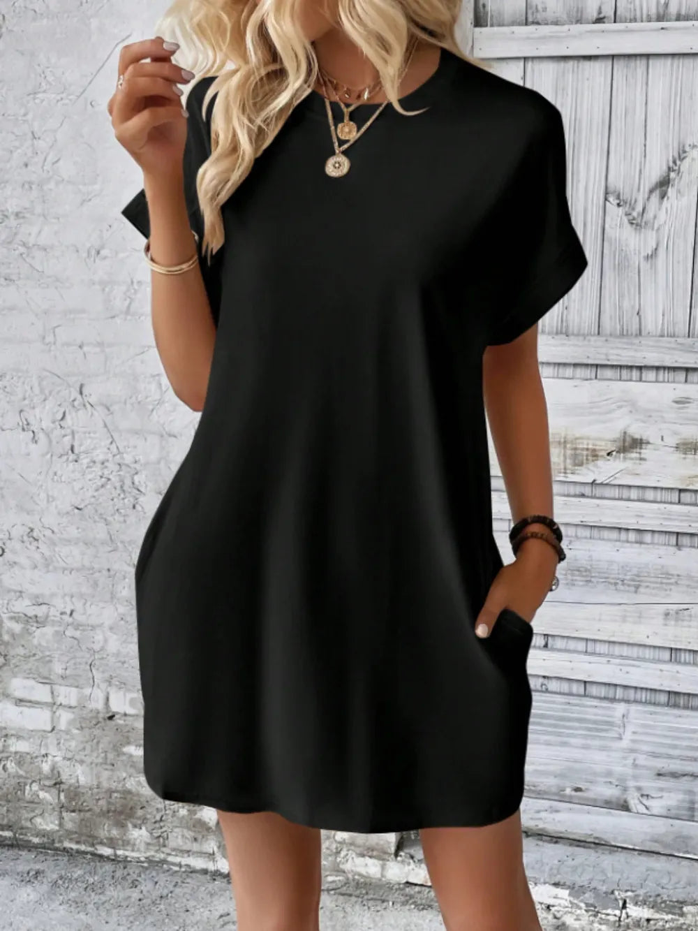 Woman wearing a black dress against a textured white wall.