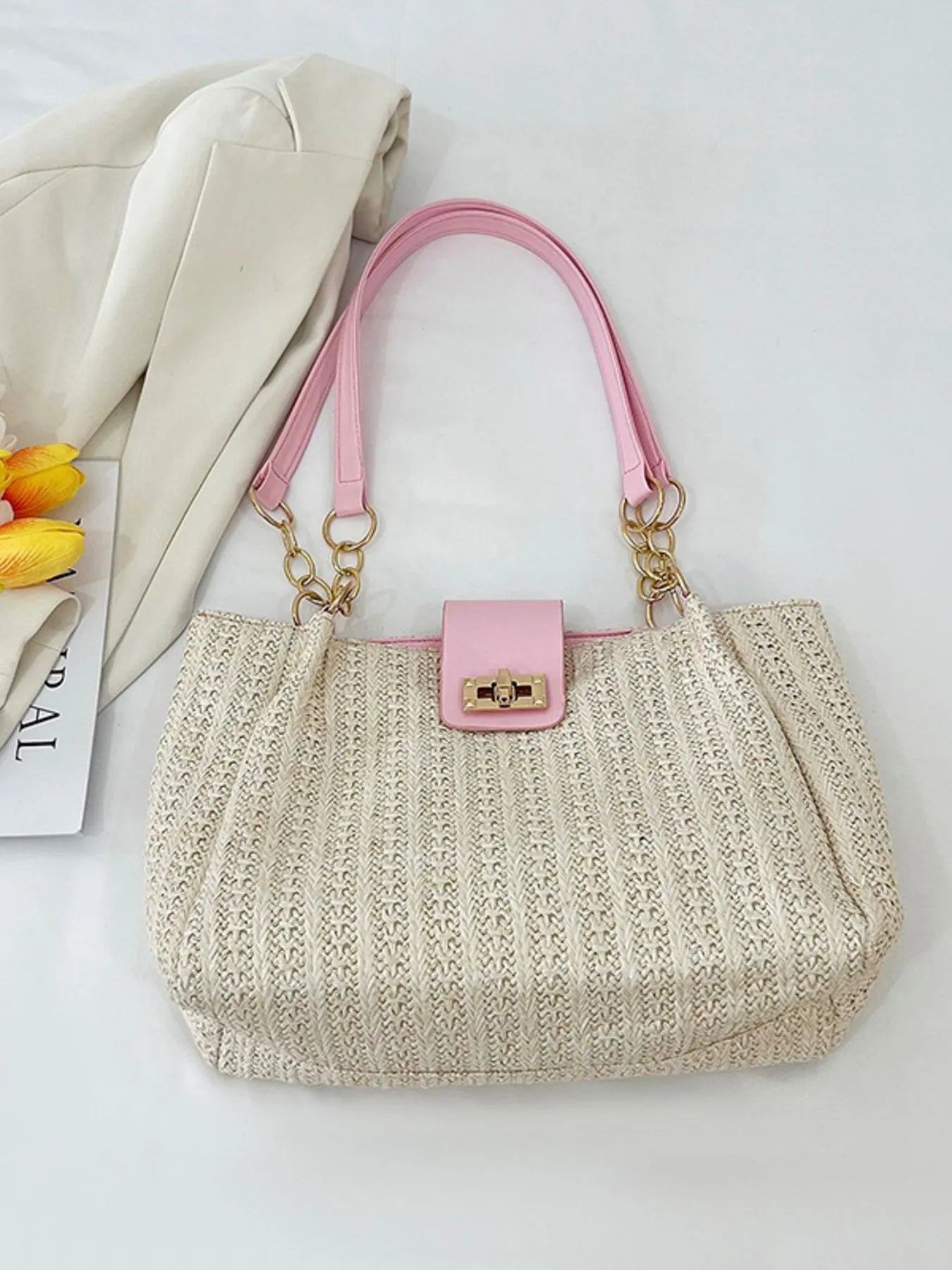 Beige woven handbag with pink handle and lock on a light background