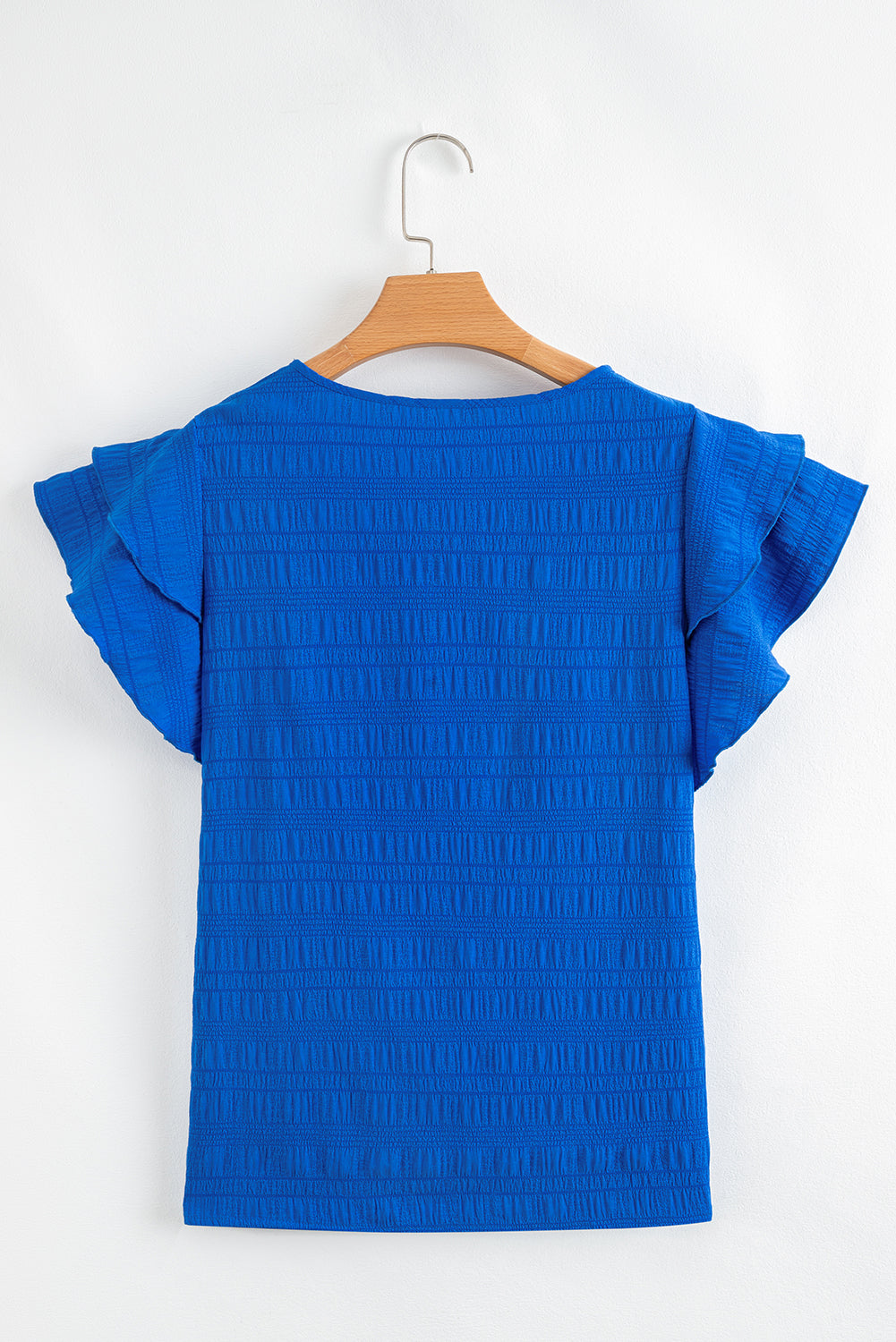 Blue textured blouse with ruffled sleeves on a wooden hanger against a white background