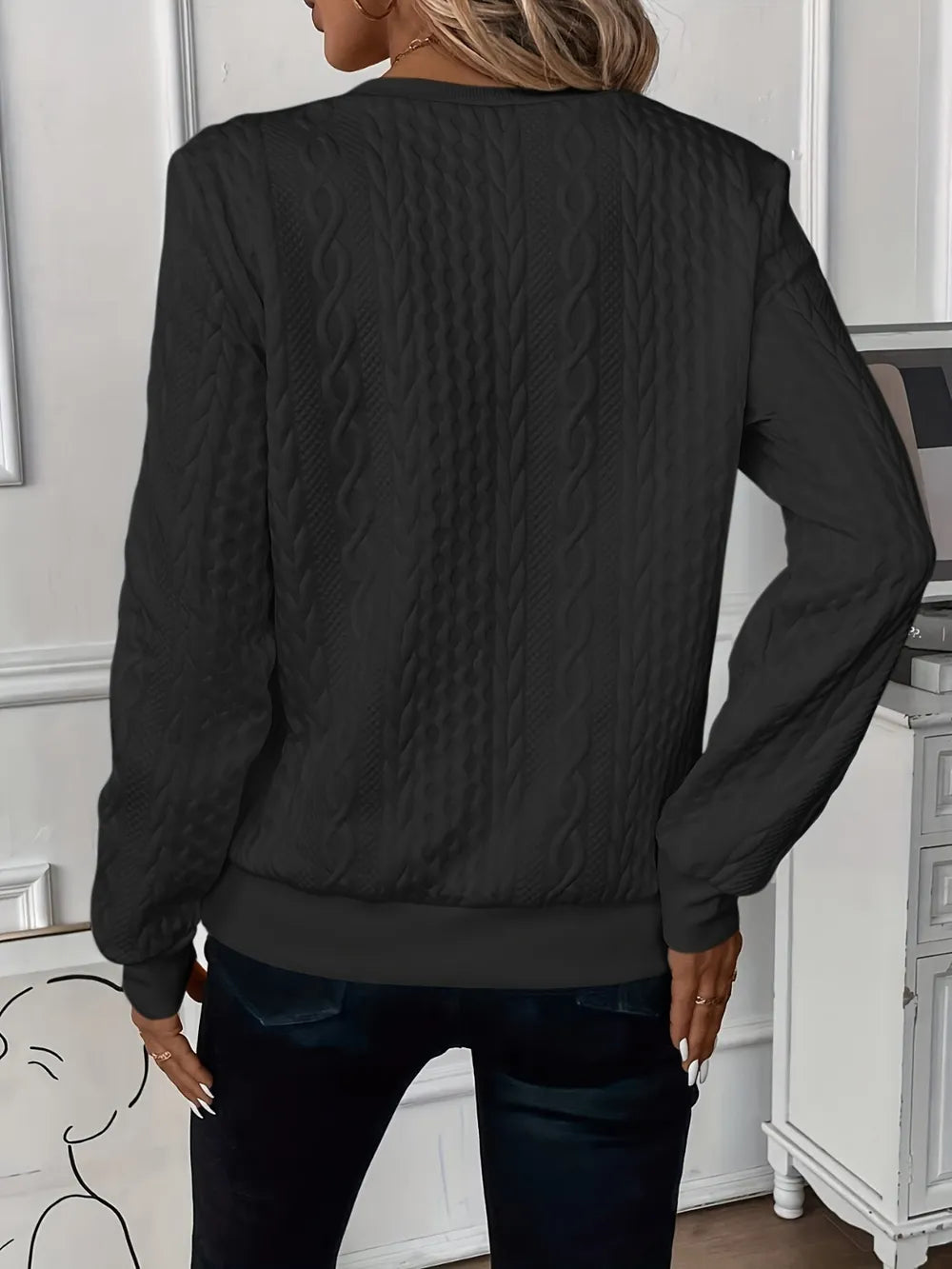 Person wearing a black textured sweater in an indoor setting