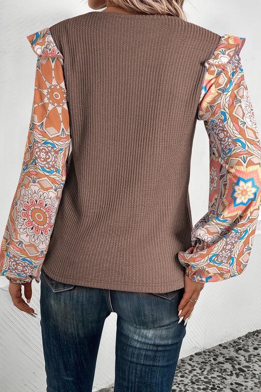 Person wearing a brown ribbed sweater over a colorful patterned shirt with blue jeans.