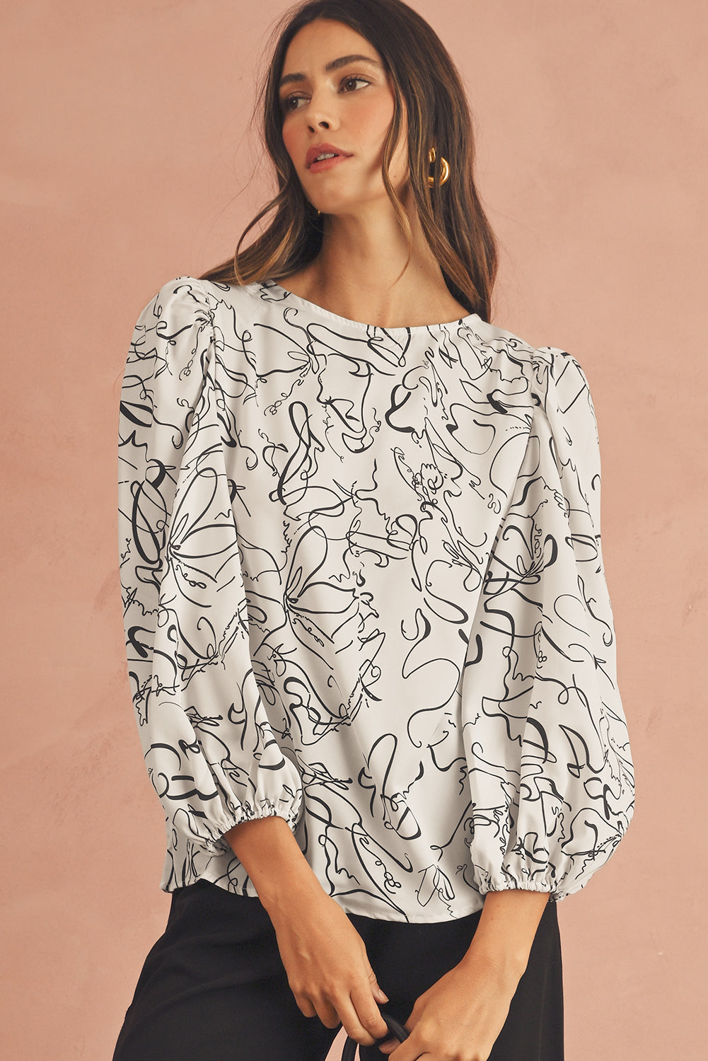 Woman wearing a white blouse with black abstract patterns on a beige background