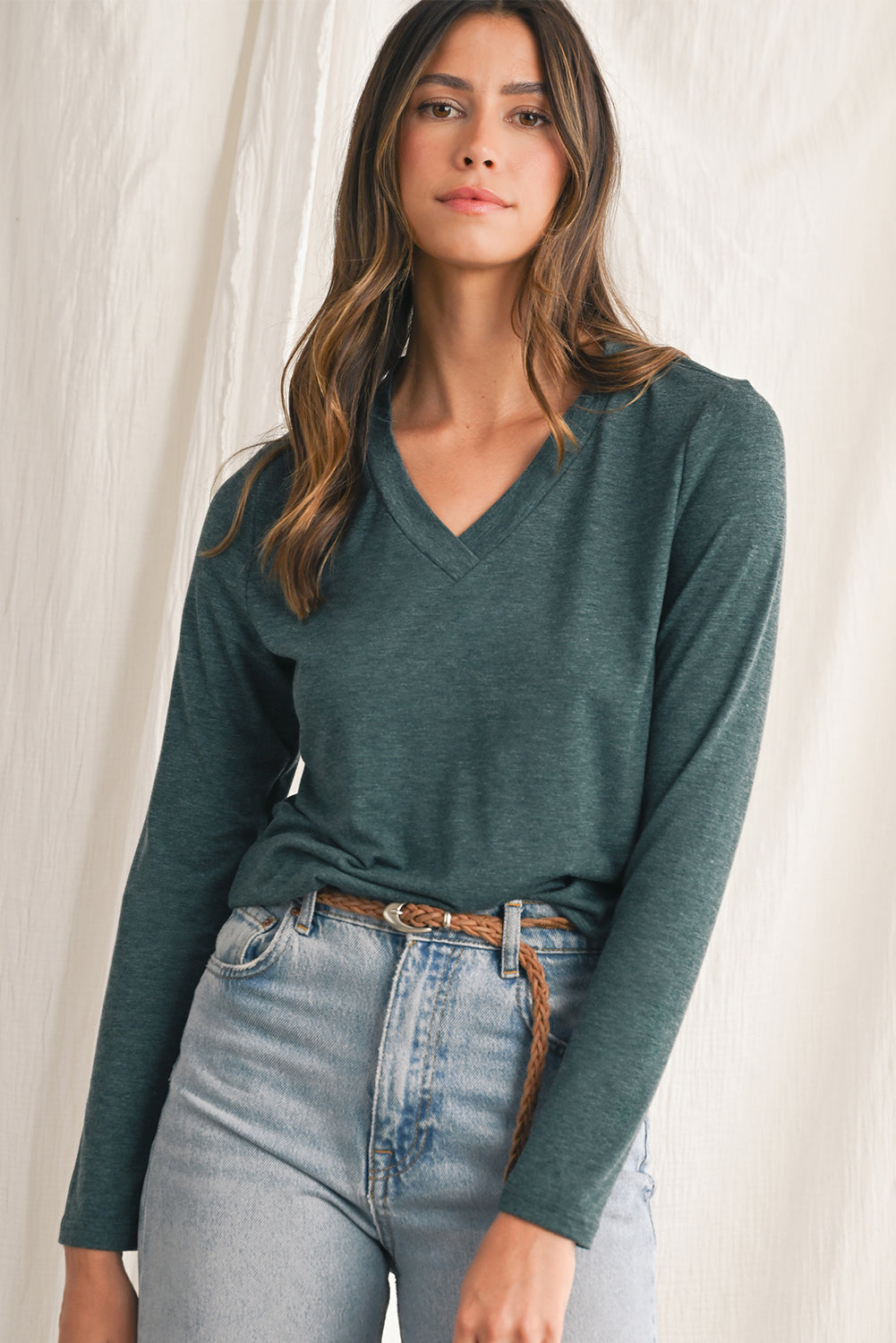 Woman wearing a green sweater and jeans against a white background
