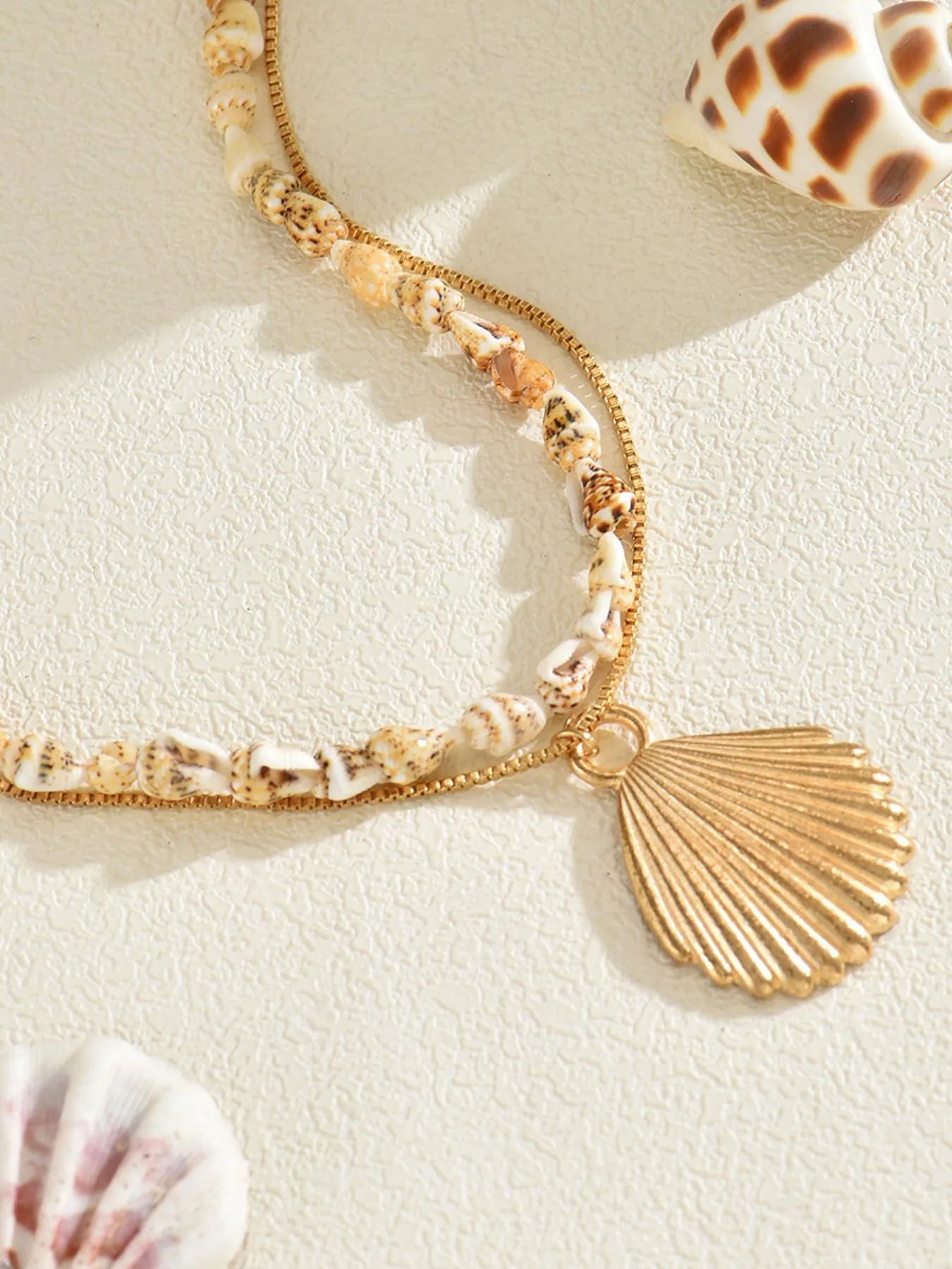 Gold necklace with shell charm on a beige background