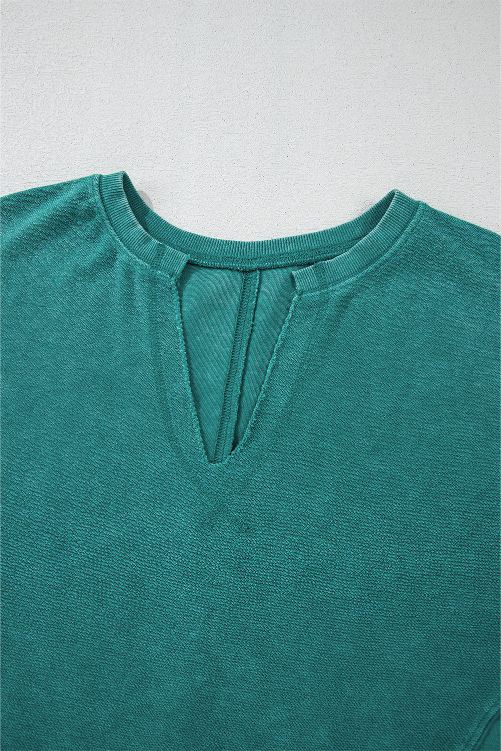 Close-up of a teal shirt with a V-neck on a light gray background