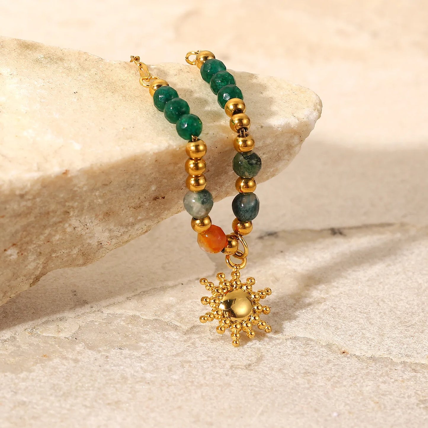 Beaded bracelet with gold sun charm on a stone surface