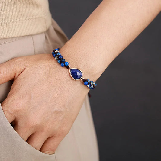 Hand wearing a blue beaded bracelet on a neutral background