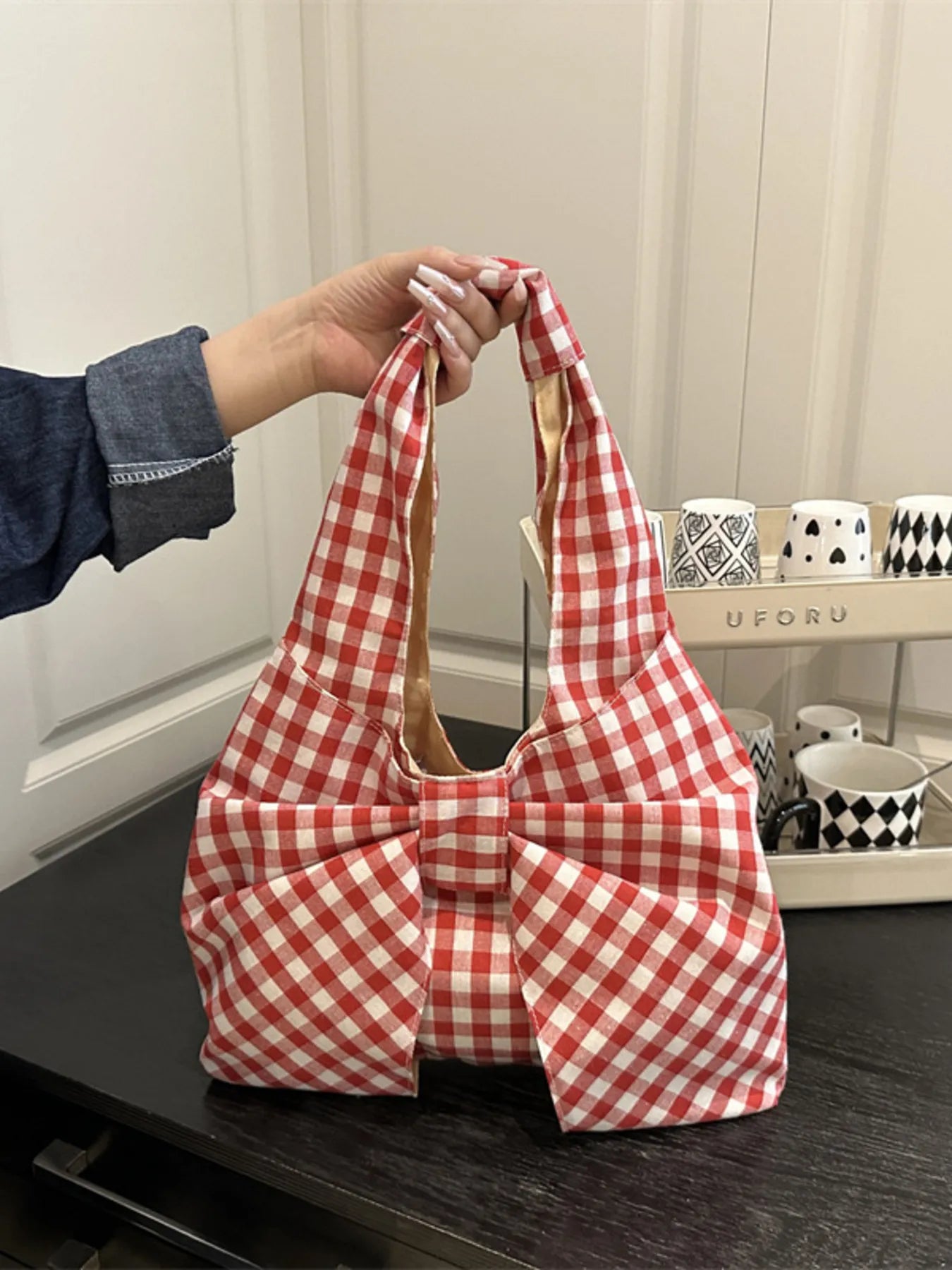 Red and white checkered bag held by a hand on a dark surface with a light-colored wall in the background.