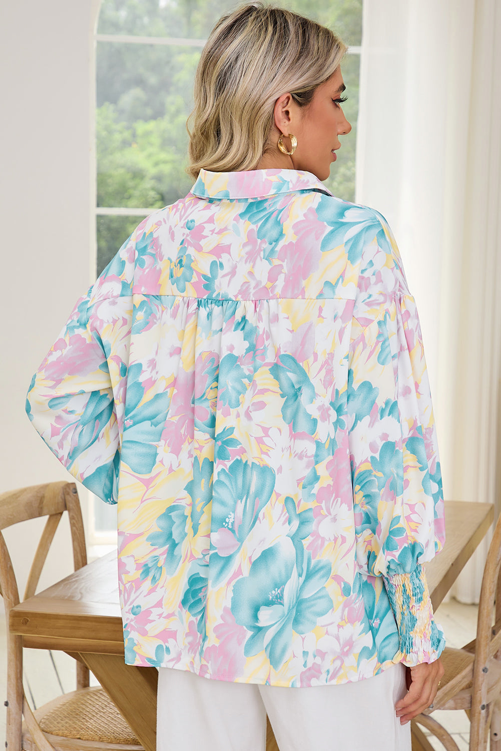 Woman wearing a colorful floral blouse in a bright room with large windows.