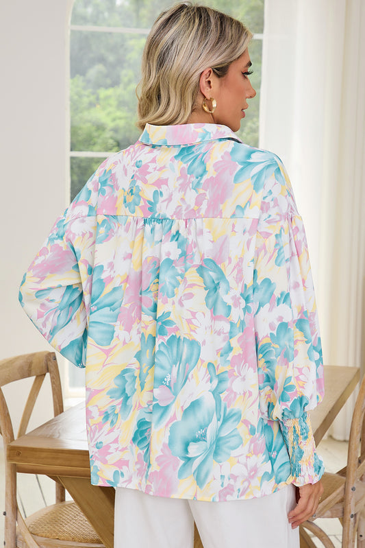 Woman wearing a colorful floral blouse in a bright room with large windows.