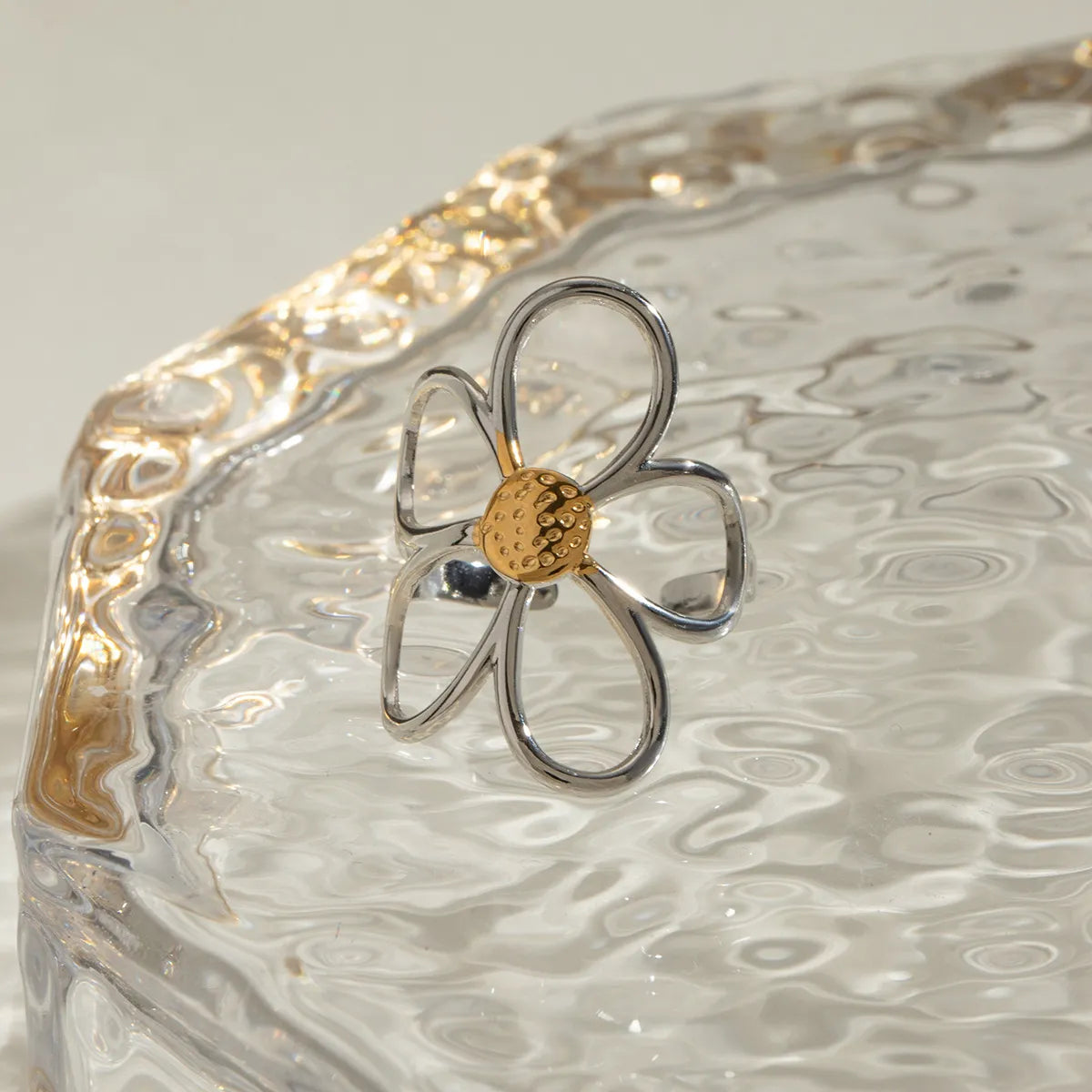 Flower-shaped jewelry piece with gold center and silver petals on a textured surface