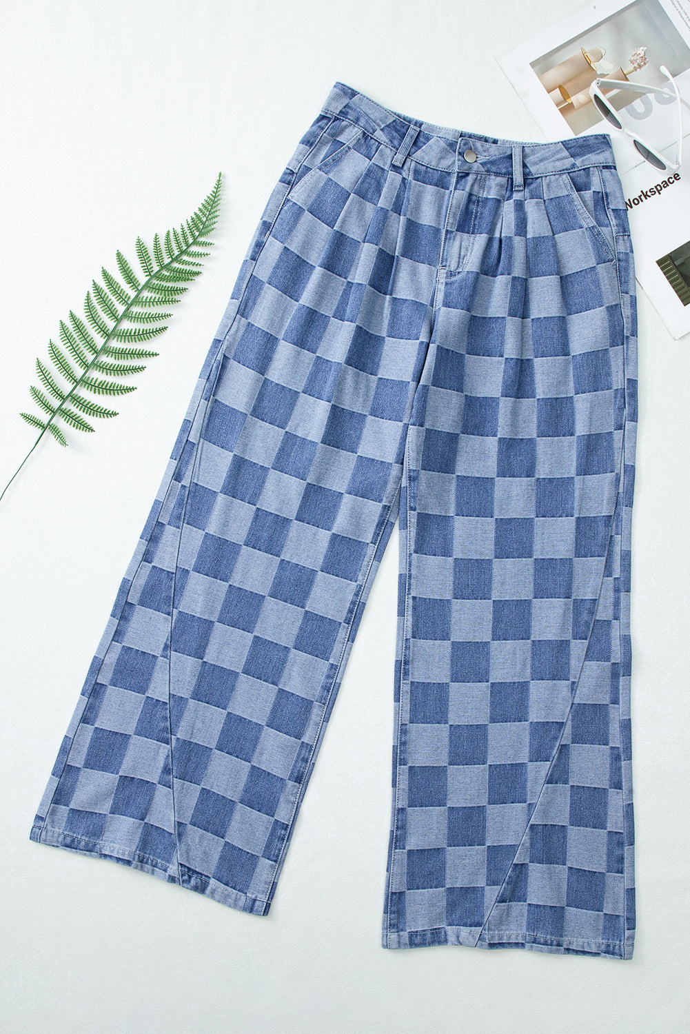 Blue checkered pants on a white background with a leaf and magazine.