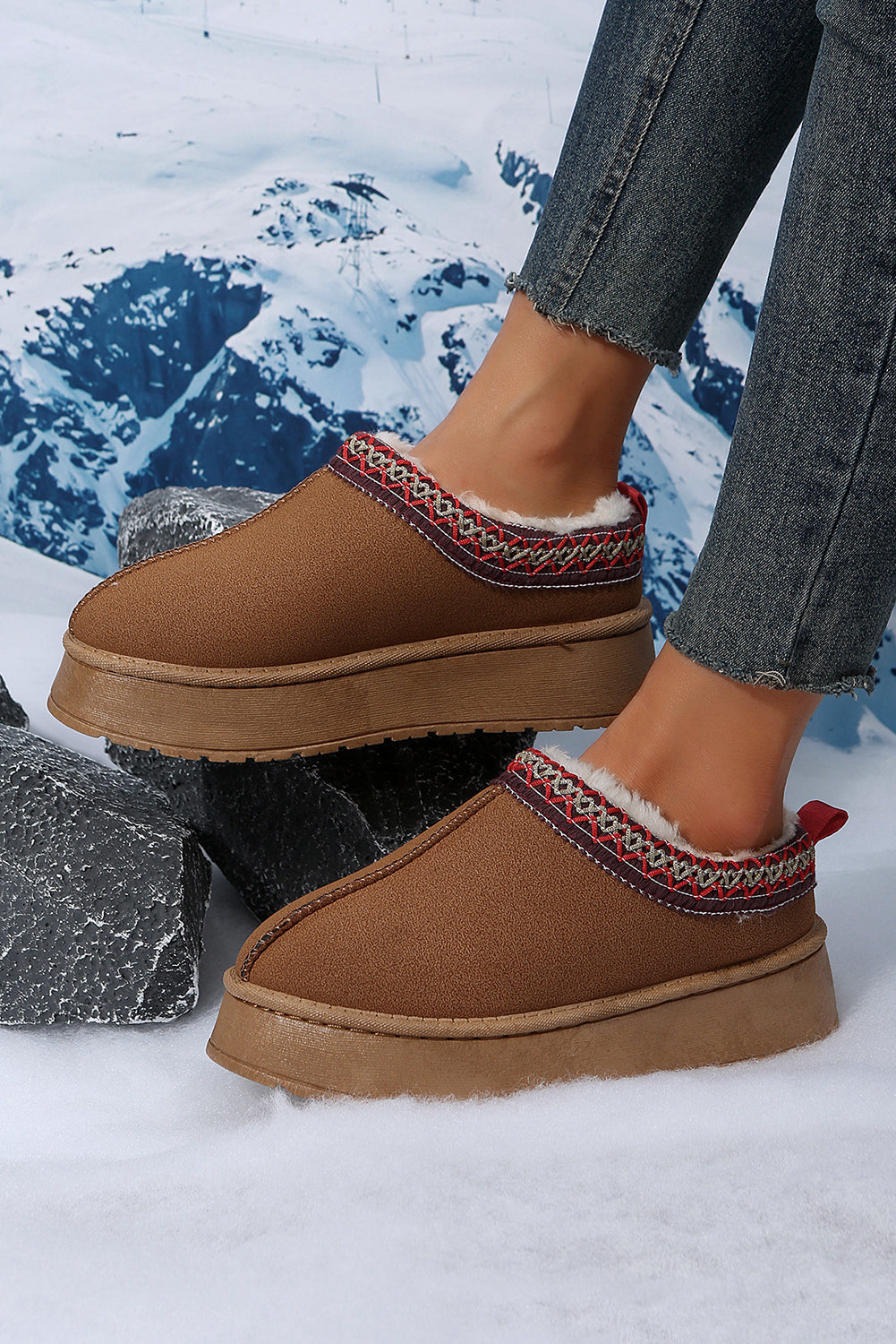 Brown slippers with decorative trim worn by a person in a snowy landscape.