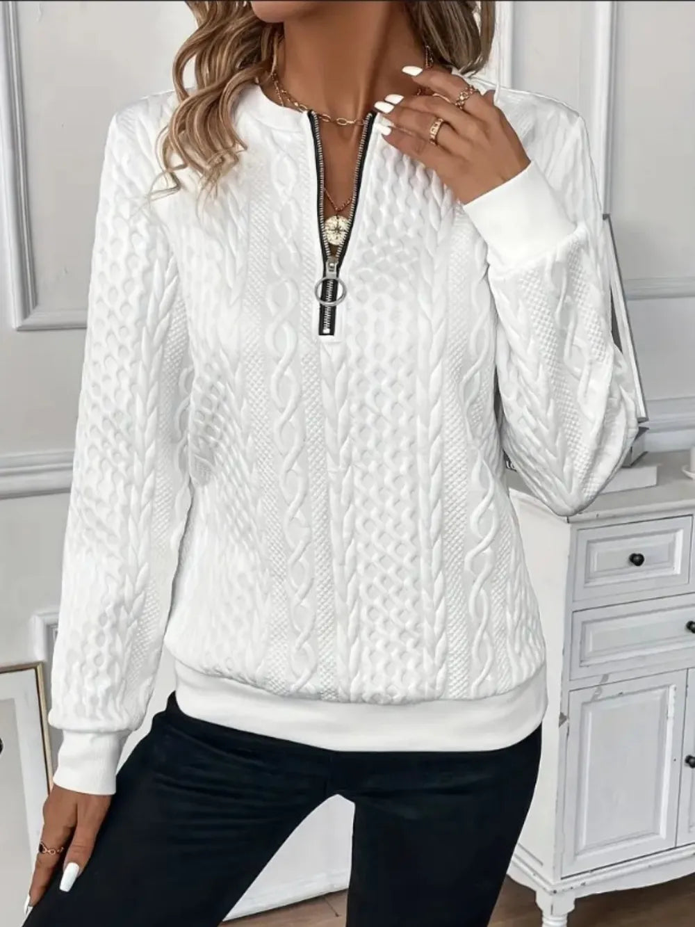 White cable knit sweater with a zipper worn by a person indoors.
