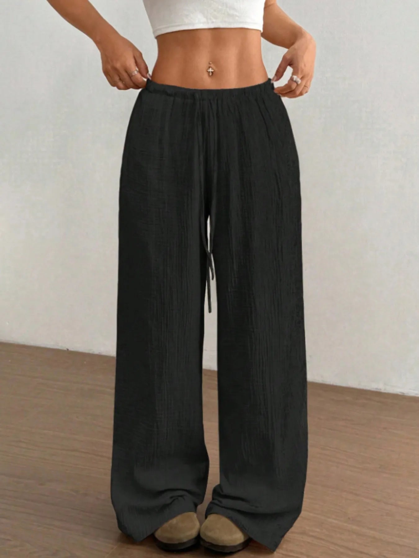 Person wearing black wide-leg pants with a white top against a plain background