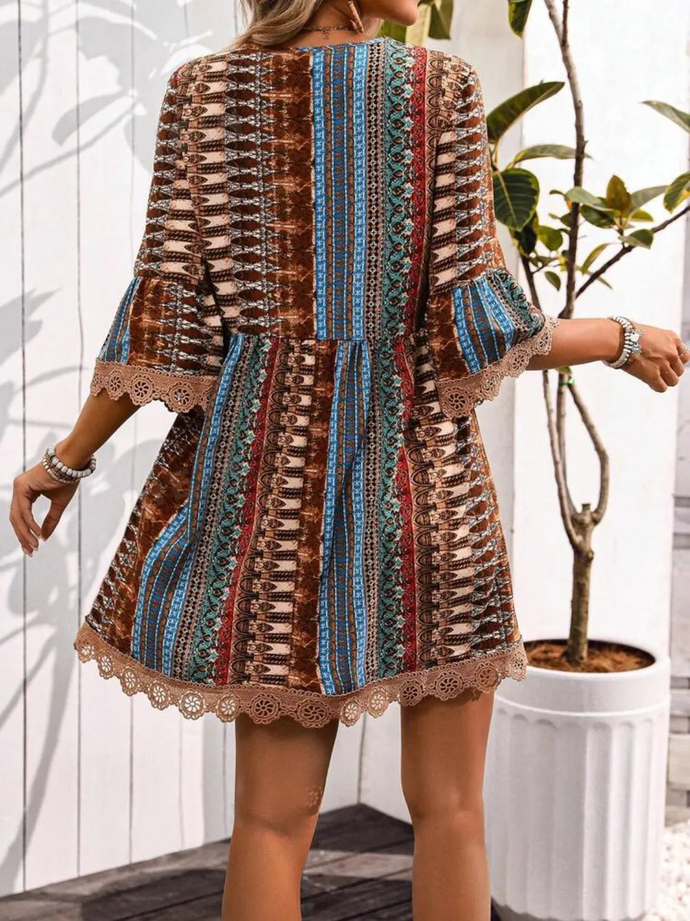 Woman wearing a patterned dress with bell sleeves in an outdoor setting.