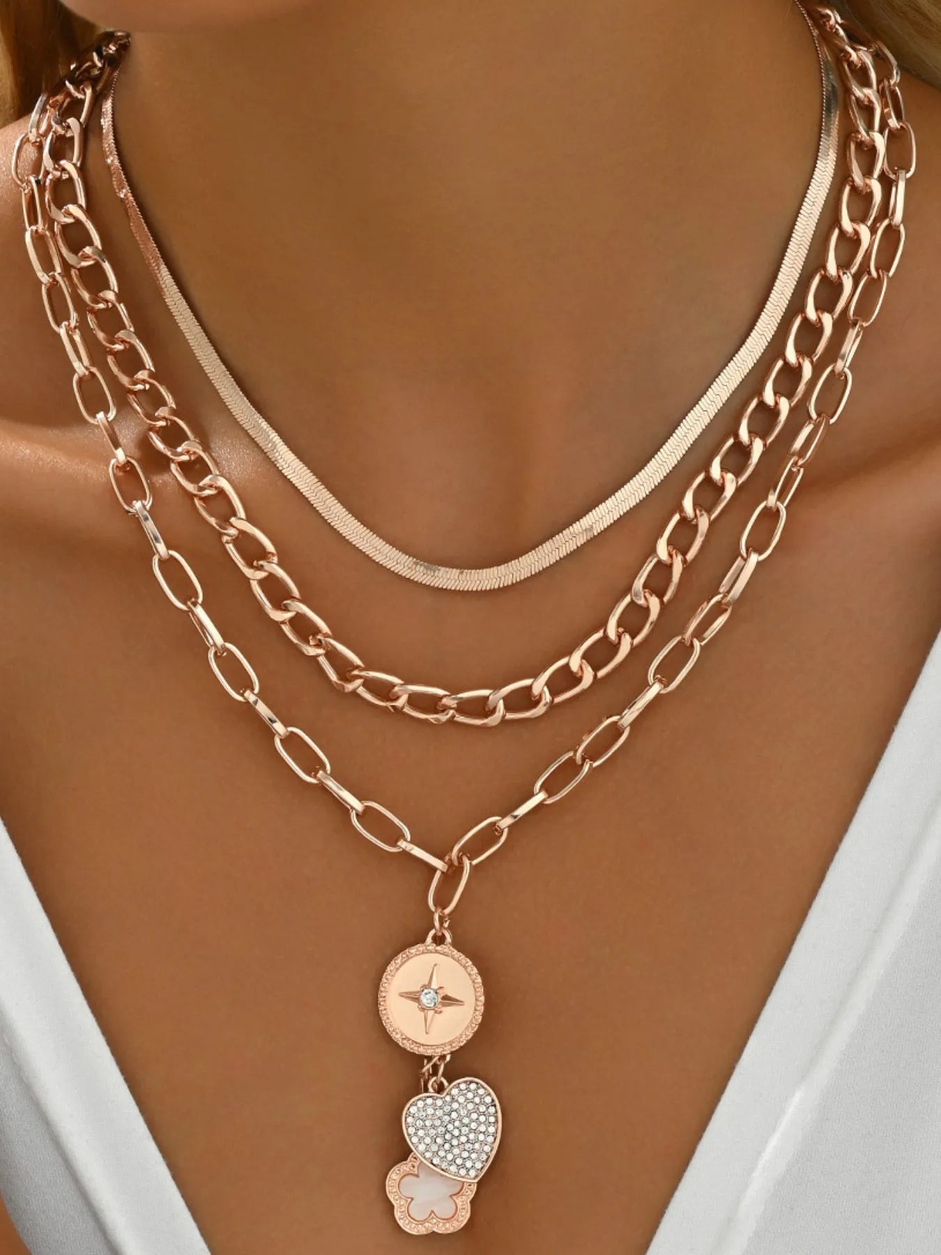 Gold chain necklace with heart and flower pendants on a model wearing a white top.