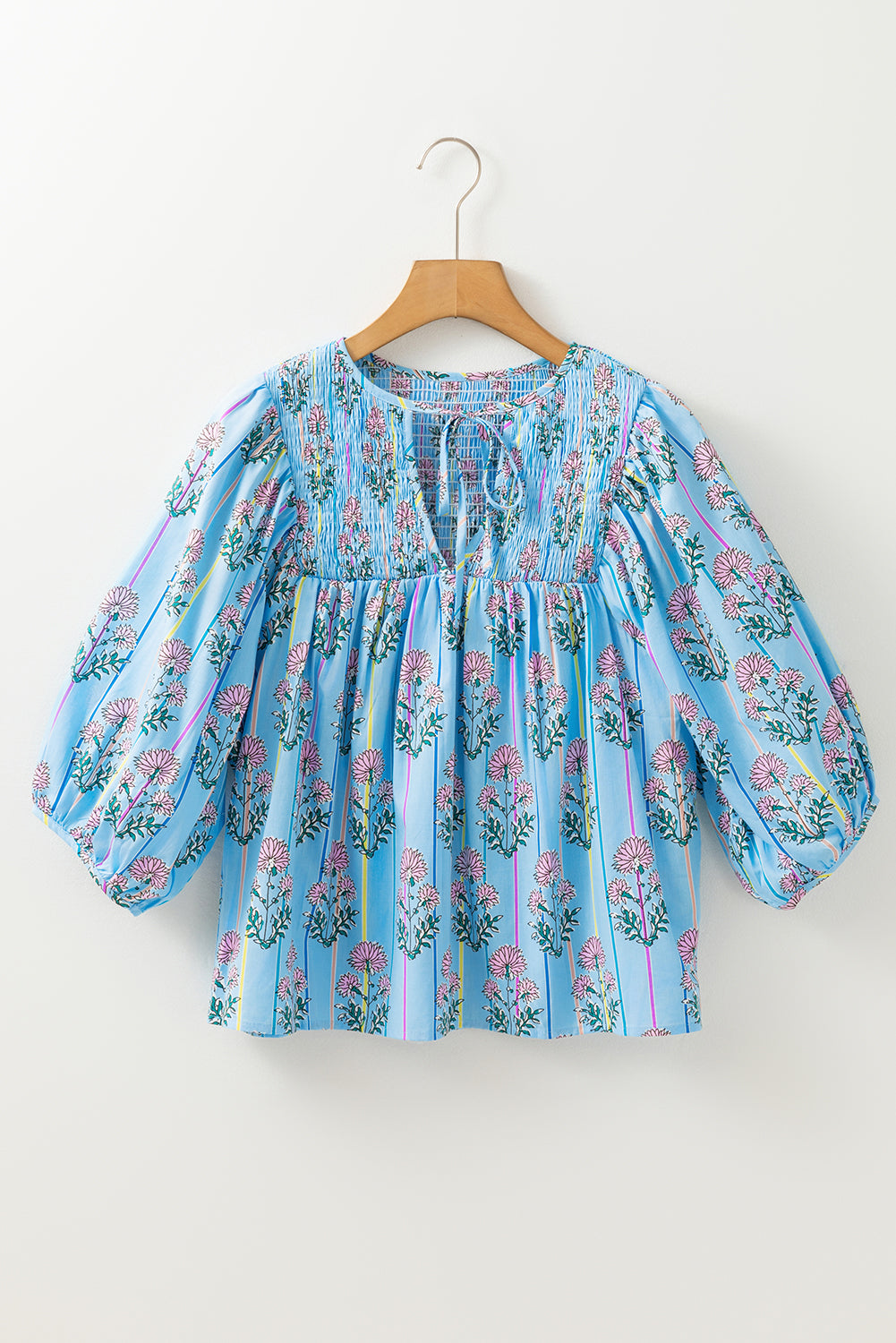 Blue floral blouse on a wooden hanger against a white background
