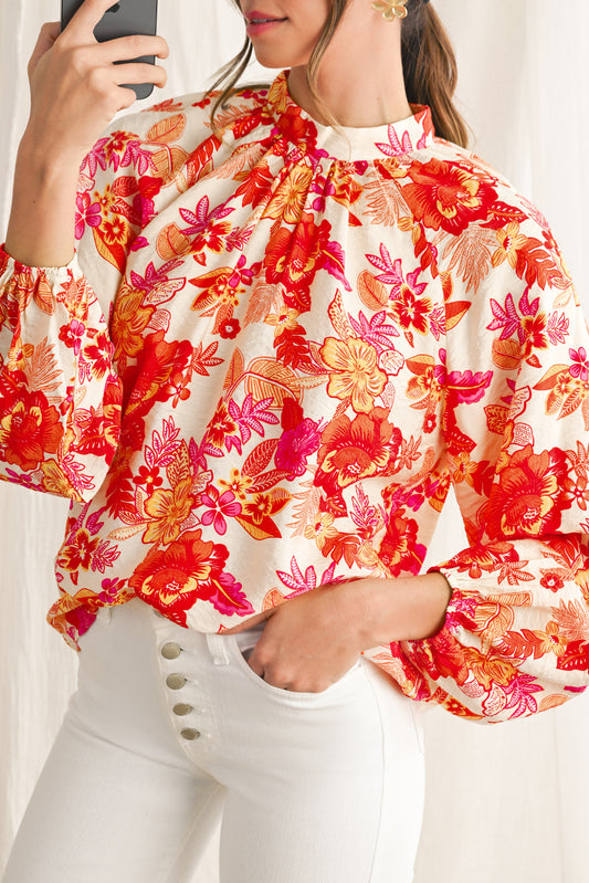 Woman wearing a colorful floral blouse with white pants.