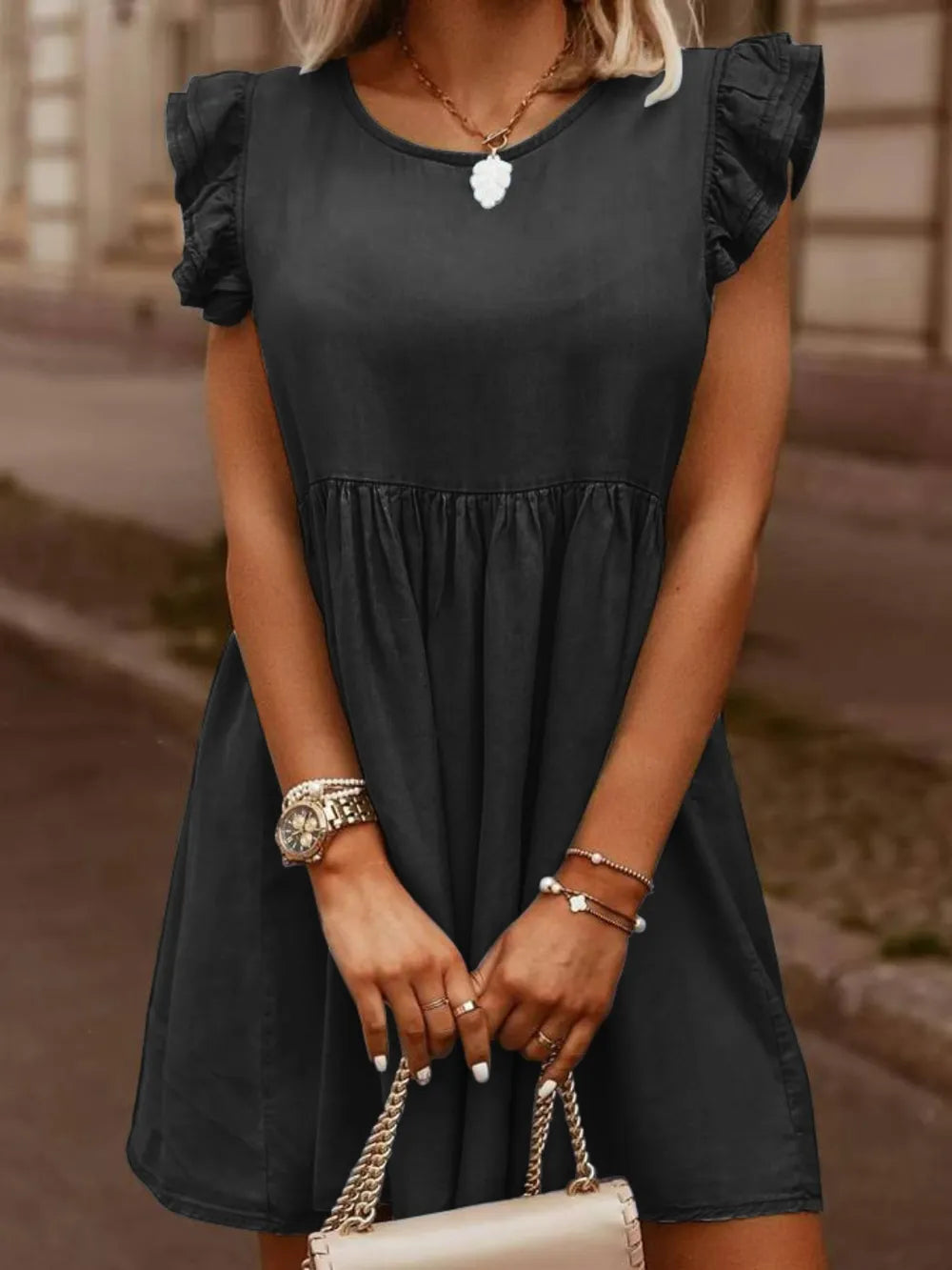 Woman wearing a black dress with ruffled sleeves, holding a beige handbag.