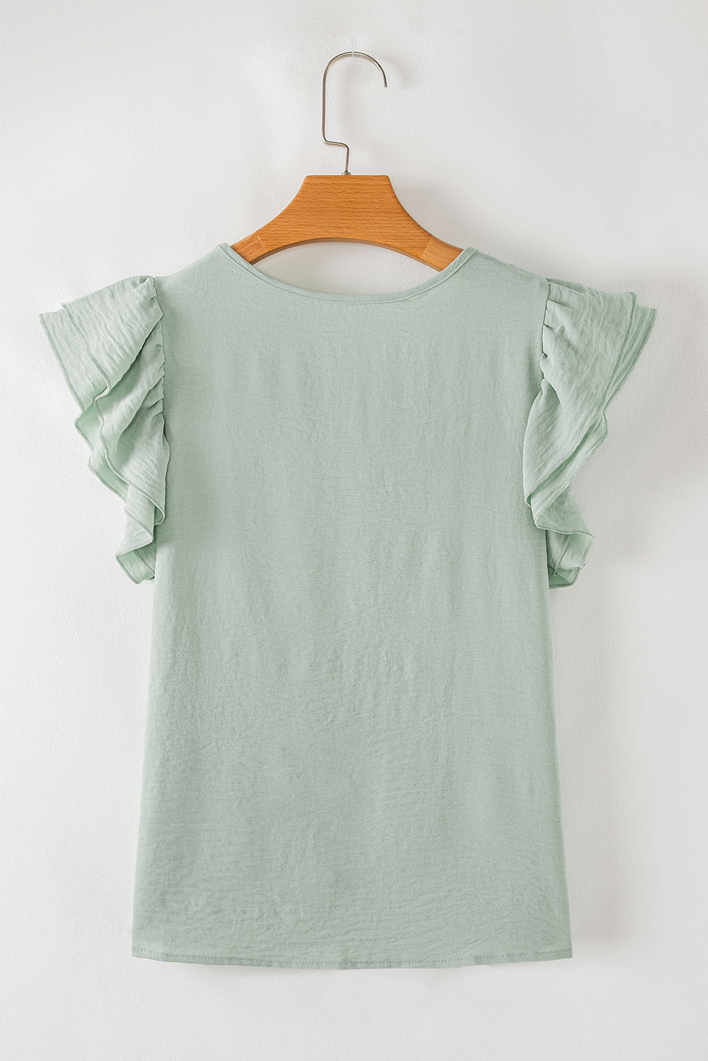 Light green dress with ruffled sleeves on a wooden hanger against a white background
