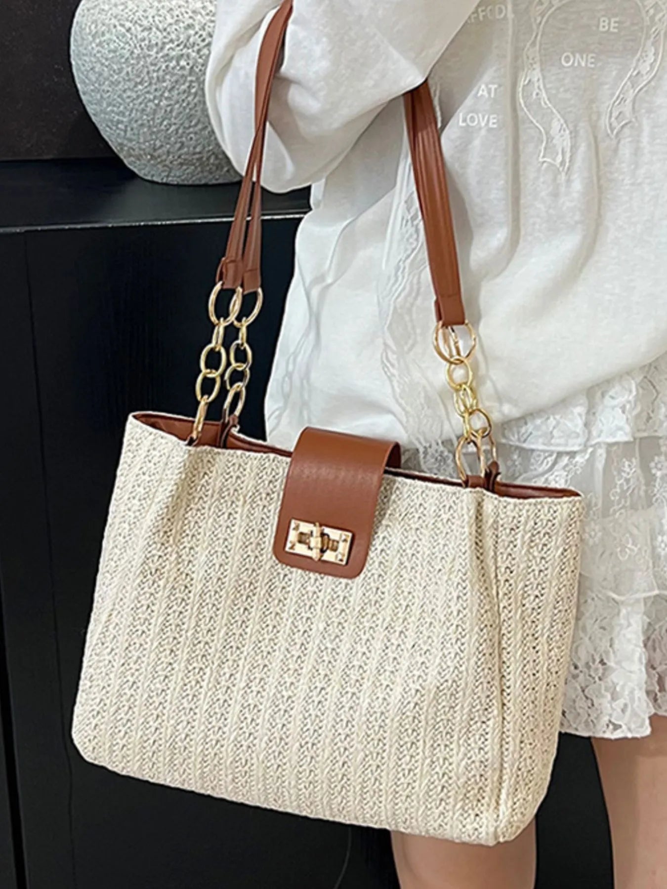 Beige handbag with brown accents held by a person wearing a white lace dress.