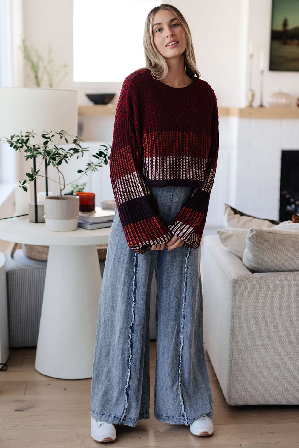 Woman wearing a striped sweater and wide-leg jeans in a living room.