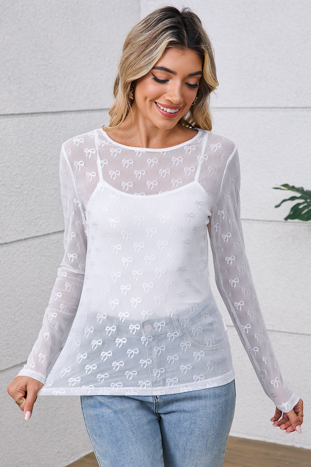 Woman wearing a white long-sleeve top with lace details against a light background